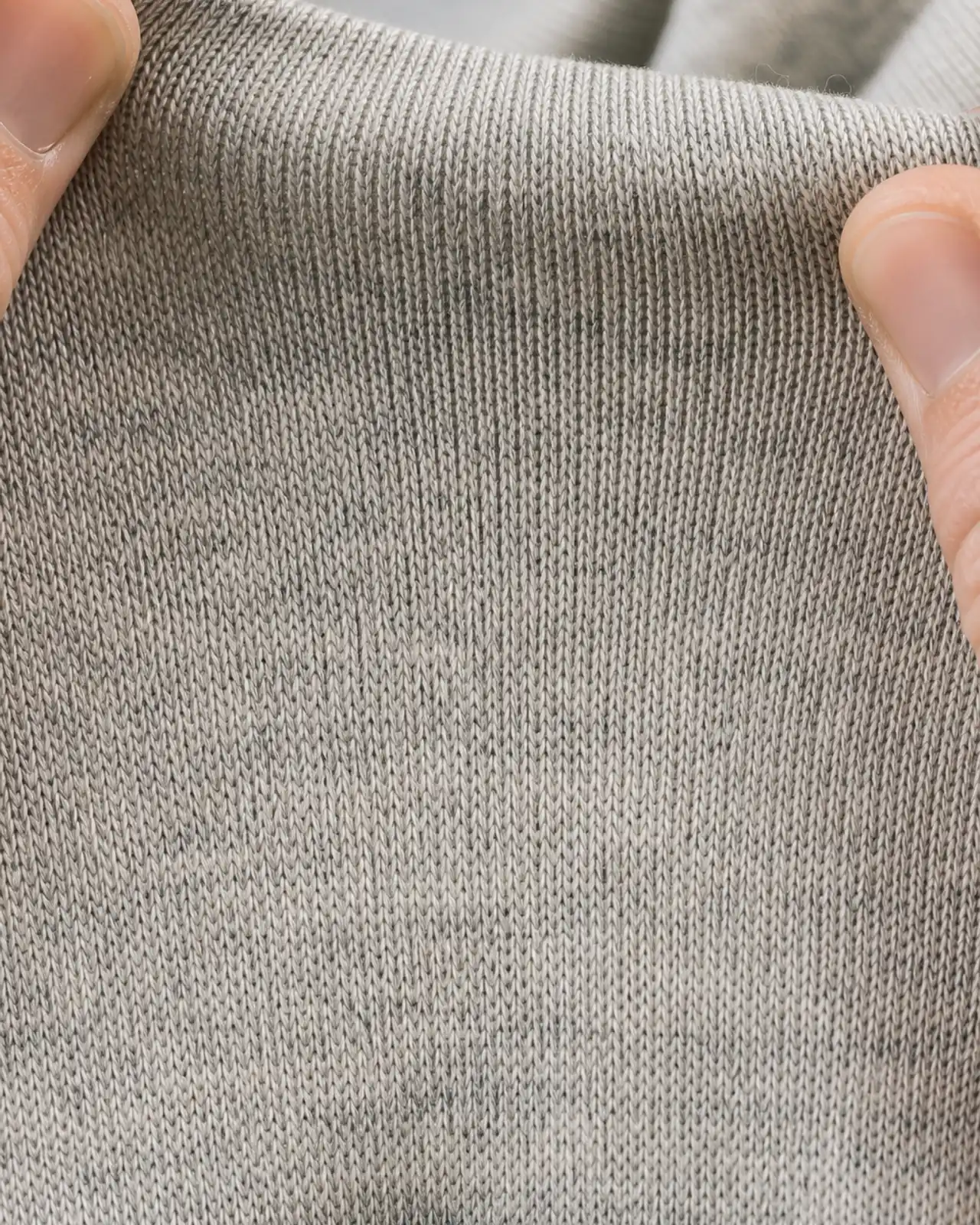 Jersey fabric close-up at roughly three times magnification, stretched between two hands to show the knit structure and recovery